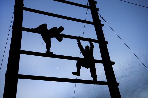 A blue background with two people in shadow, climbing up an obstacle structure.