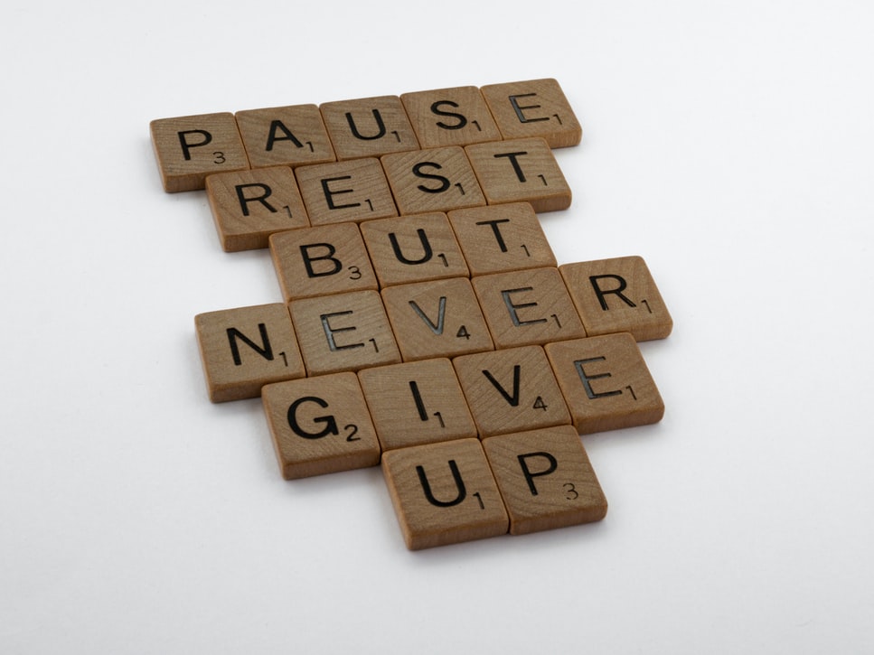 Scrabble tiles on a white table that says pause, rest, but never give up.